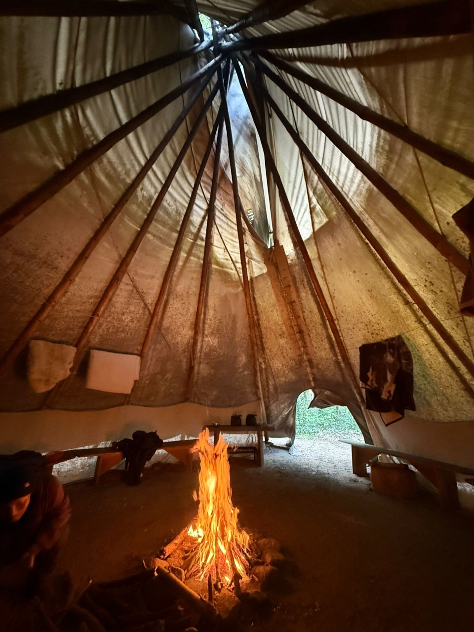 Blick ins Tipi mit Lagerfeuer und Sitzbänken auf dem Kursgelände