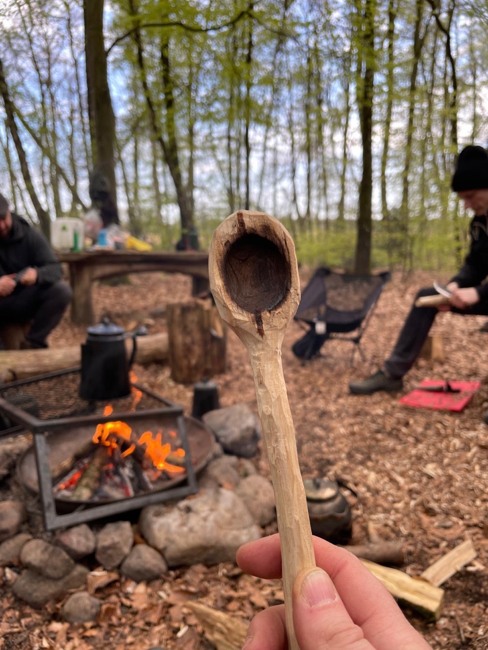 Selbst geschnitzter Holzlöffel vor der Feuerstelle im Wald